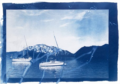 Zwei Segelboote schwimmen auf einem blauen Gewässer vor schneebedeckten Bergen.