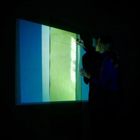 Eine Person projektiert farbige Lichtstreifen auf eine Wand.