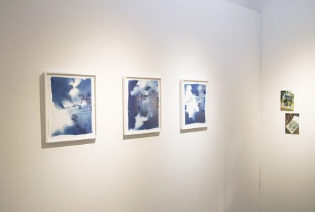 Drei gerahmte Kunstwerke in Blau- und Grautönen an einer hellen Wand.