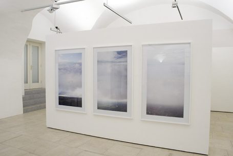 Drei rahmene Bilder in sanften Farbtönen an einer weißen Wand in einer Galerie.