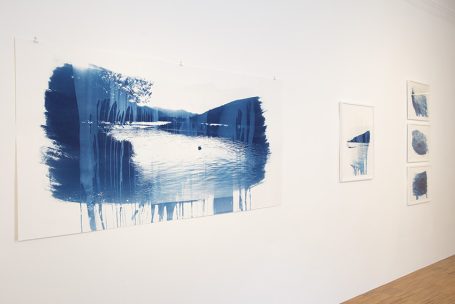 Blaues Landschaftsbild mit Wasser, Bäumen und sanften Hügeln, hängend an einer Wand.