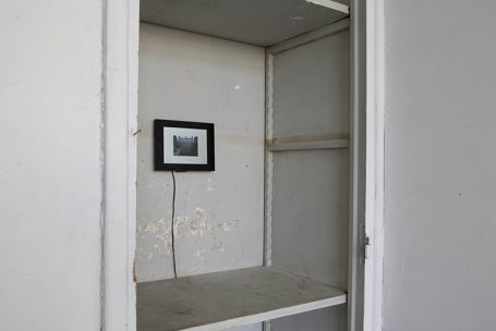 Leerer Schrank mit einem kleinen Bild an der Wand und sichtbaren Wandschäden.