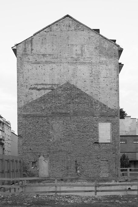 Graue, unverputzte Gebäudewand mit einem dreieckigen Schatten und einem Fenster.