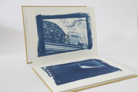 Buch mit zwei Seiten, eine zeigt eine blaue Landschaft, die andere ein dunkles Rechteck.