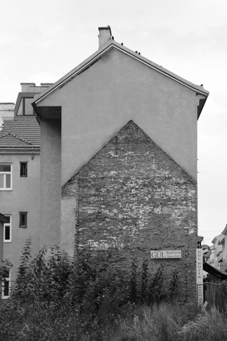 Graues Gebäude mit einer markanten Wandstruktur und Pflanzen im Vordergrund.