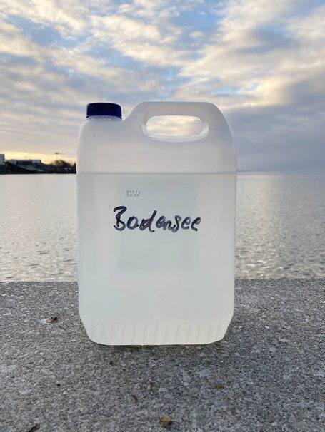 Ein milchiger Wasserbehälter mit der Aufschrift "Bodensee" vor einem Seehorizont.