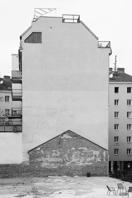 Eine graue, schlichte Hauswand mit unregelmäßiger Form und Sicht auf unvollendete Bereiche.