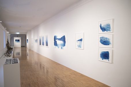 Weißer Ausstellungsraum mit blauen aquarellartigen Kunstwerken an den Wänden.
