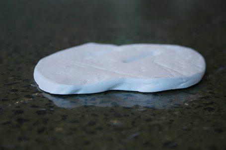Weiße Knetmasse liegt auf einer dunklen, glatten Oberfläche.