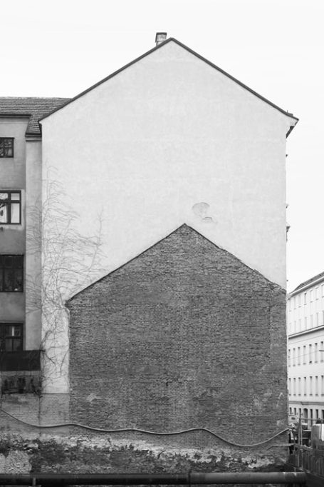 Hinteransicht eines Gebäudes mit weißer und roter Mauer, teilweise verwittert.