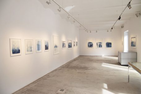 Moderne Galerie mit blauen Kunstwerken an weißen Wänden und hellem Boden.