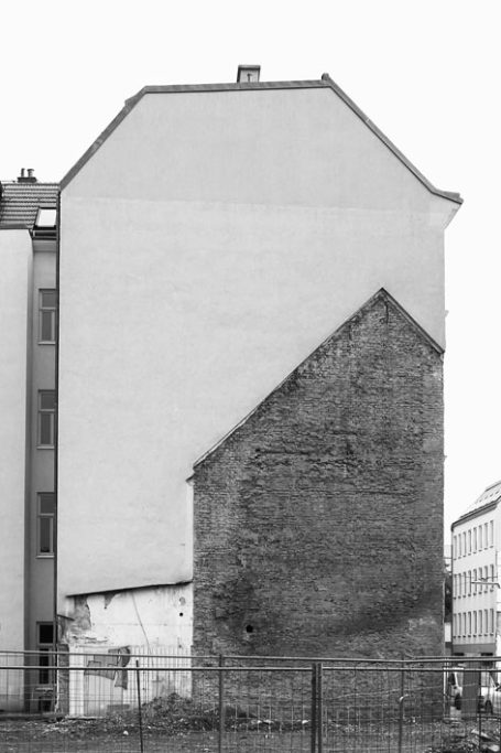 Hinteransicht eines Gebäudes mit einer modernen weißen Wand und einem alten Steinsockel.