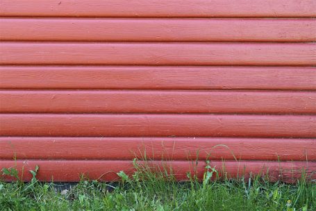 Rote Wand mit horizontalen Streifen und grünem Gras im unteren Bereich.