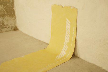Gelbes, gestreiftes Papier liegt an der Wand, mit einer rauen, texturierten Oberfläche.
