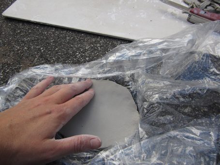 Eine Hand formt graues Tonmaterial, umgeben von Plastikfolie.