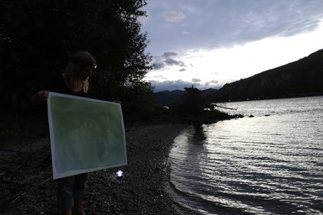 Person hält eine Karte am Ufer eines ruhigen Sees bei Dämmerung.