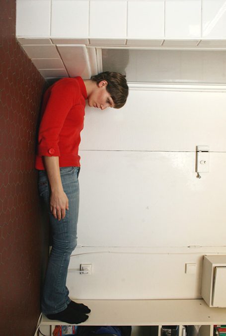 Junger Mensch in rotem Shirt, lehnt mit dem Kopf an einer Wand.