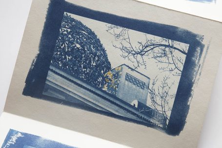 Blaues Bild eines Gebäudes mit Bäumen und einem Felsen im Hintergrund.
