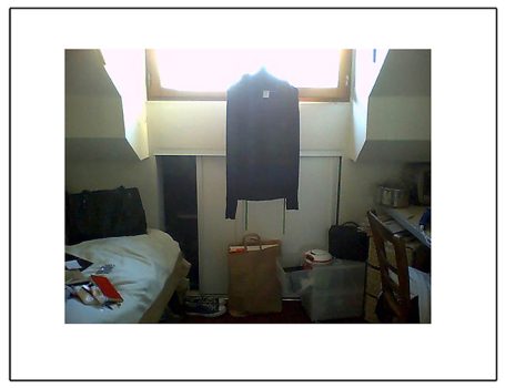 Ein kleiner Raum mit einem Bett, einem Kleiderschrank und einem hängenden Kleidungsstück.