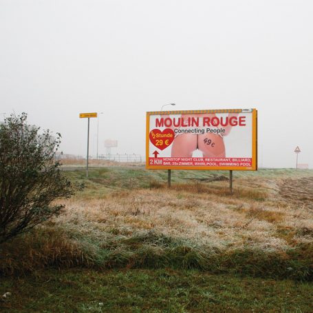 Werbeschild für Moulin Rouge in nebliger Landschaft mit Gras.