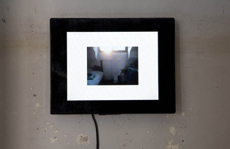 Ein gerahmtes Bild auf einer Wand zeigt eine unscharfe Innenszene mit Licht.