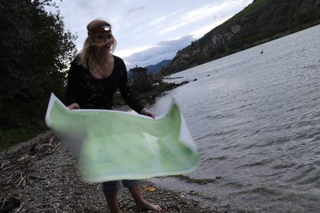 Frau hält eine Karte am Ufer eines Gewässers, umgeben von Natur.