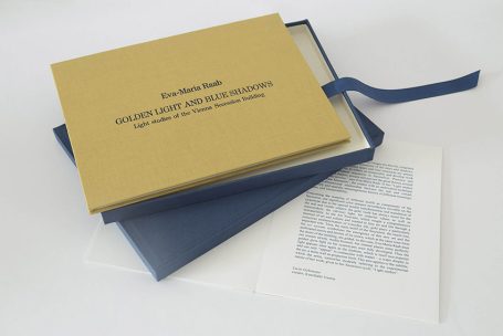Ein geschlossenes Buch in einer blauen Hülle, daneben ein Dokument mit Text.