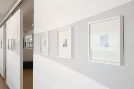 Weißer Innenraum mit gerahmten, minimalistischen Kunstwerken an der Wand.