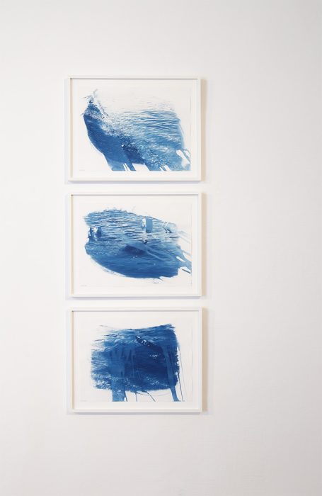 Drei gerahmte Kunstwerke mit abstrakten blauen Pinselstrichen an einer Wand.