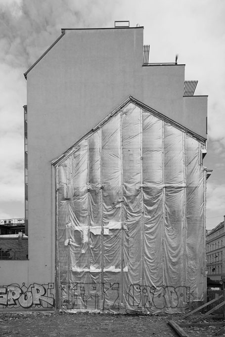 Graue Gebäudeansicht mit eingewickelter, faltiger Fassade in der unteren Hälfte.