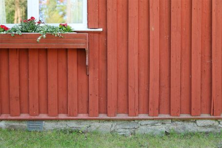 Rote Holzverkleidung mit Blumenkasten und grüner Wiese im Vordergrund.