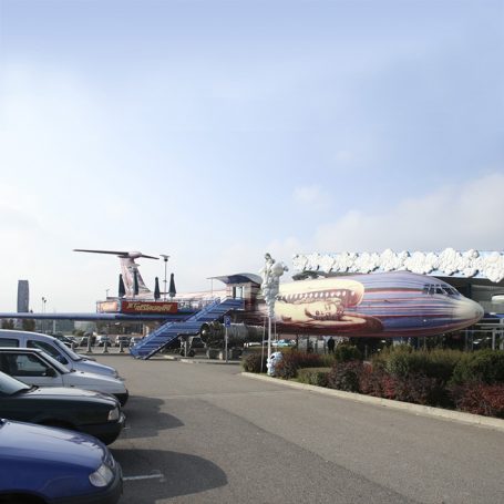 Ein alte Flugzeugattraktion mit rotem und blauem Design neben einem Parkplatz.