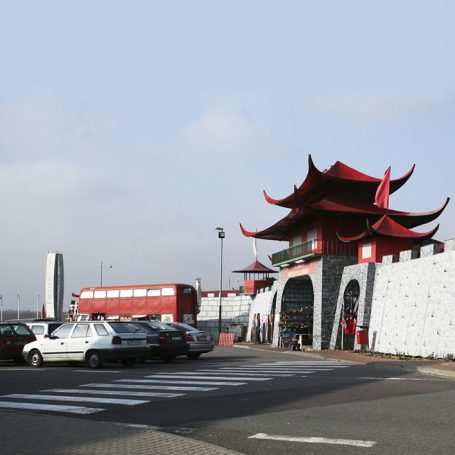 Chinesisches Tor mit rotem Dach, umgeben von Mauern und parkenden Autos.