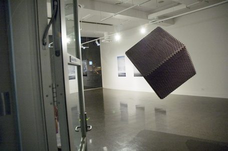 Ein schwebender, rotbrauner Würfel in einem modernen Ausstellungsraum.