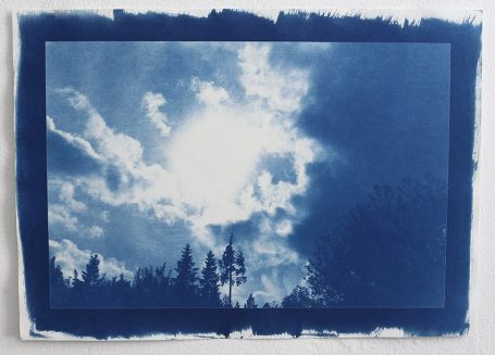 Himmel mit Wolken und Sonne über silhouettierten Bäumen im Vordergrund.