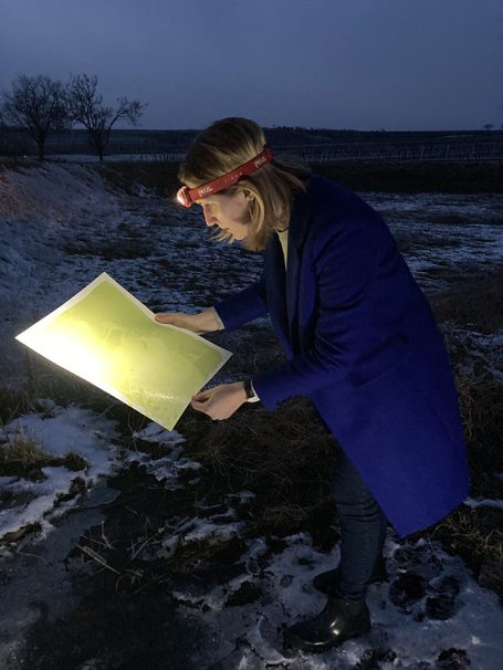 Eine Person mit Stirnlampe untersucht ein gelbes Blatt Papier im Freien bei Dämmerung.