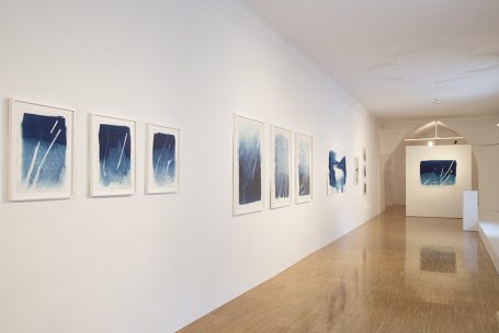 Kunstgalerie mit blauen Kunstwerken an weißen Wänden und einem hellen Boden.
