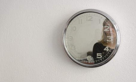 Runder Spiegel an einer Wand, reflektiert eine Person und hat eine skalenartige Darstellung.