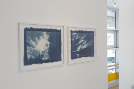 Zwei blaue Kunstwerke in weißen Rahmen, an einer hellen Wand hängend.