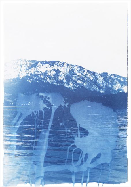 Berglandschaft mit blauen Farbtönen und reflektierendem Gewässer im Vordergrund.