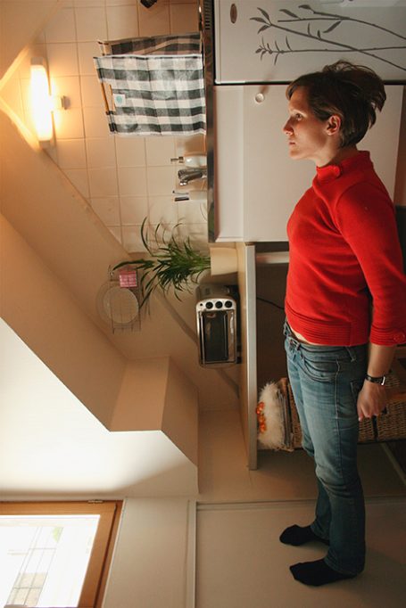Frau in rotem Pullover steht in einer hellen Küche neben einer Pflanze.