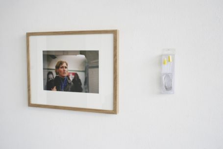 Ein gerahmtes Porträt einer Person neben einem grauen Wandobjekt.
