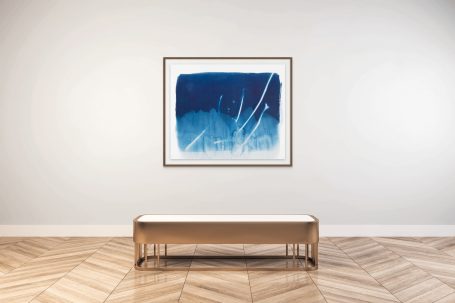 Blaues abstraktes Kunstwerk in einem Rahmen über einer minimalistischen Holzbank.