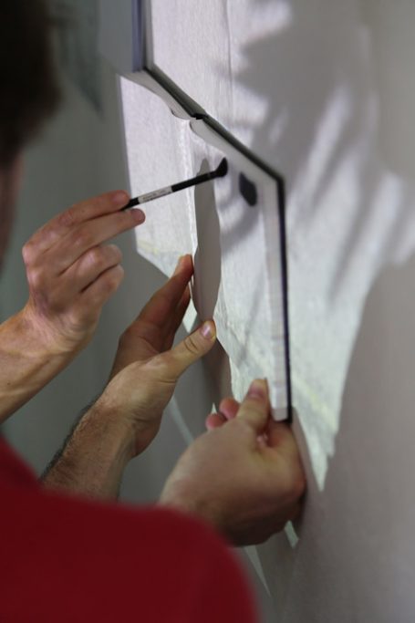 Hände halten einen Rahmen an der Wand, während ein Stift zur Markierung benutzt wird.