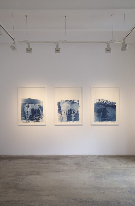 Drei blaue Kunstwerke an einer weißen Wand in einer Galerie.