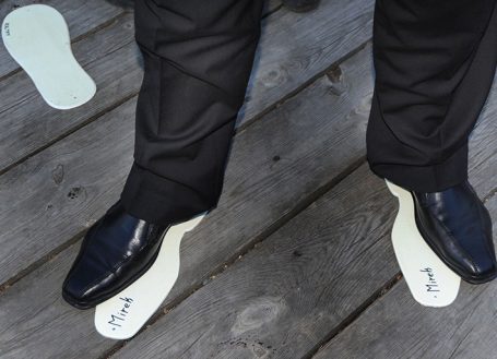 Schwarze Schuhe mit herausgenommenen Einlagen auf einem Holzboden.