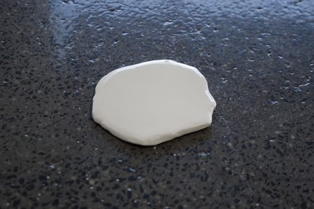 Ein flacher, weißer Keks auf einer dunkelgrauen Oberfläche.