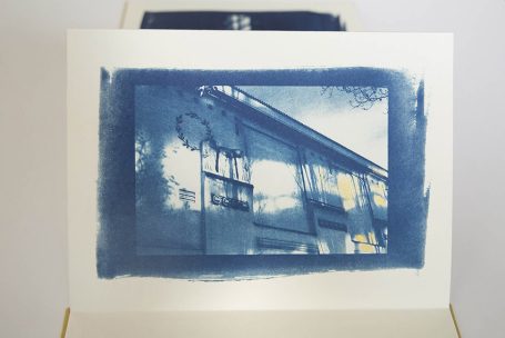 Ein cyanotypisches Bild eines Hauses mit Bäumen im Hintergrund und unregelmäßiger Umrandung.
