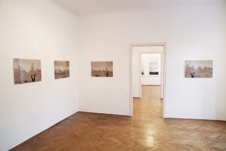 Moderne Galerie mit mehreren Bildern an weißen Wänden und einem Fenster im Hintergrund.