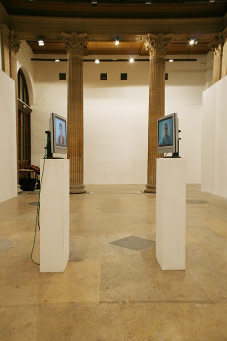 Zwei Computer auf Säulen in einem modernen Ausstellungsraum mit Säulen im Hintergrund.